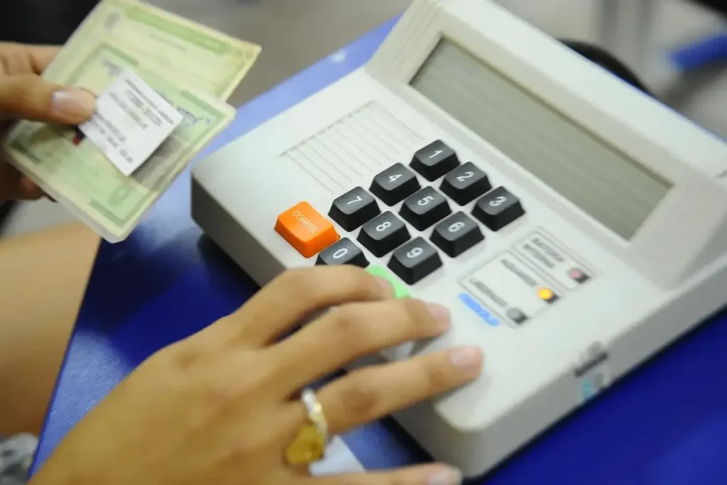 Pessoa votando em equipamento de votação eleitoral, ilustrando o processo de regularização do título eleitoral e os prazos para as eleições de 2026.