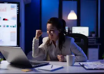 Mulher comemorando produtividade em frente ao laptop, simbolizando a regra dos 80% aplicada no trabalho.