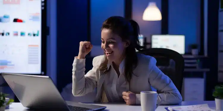 Mulher comemorando produtividade em frente ao laptop, simbolizando a regra dos 80% aplicada no trabalho.