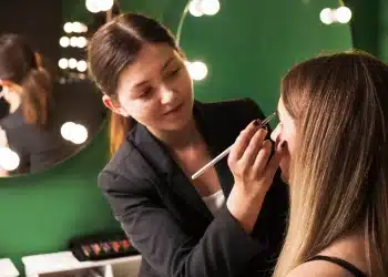 Profissional de beleza aplicando maquiagem em cliente em estúdio iluminado.