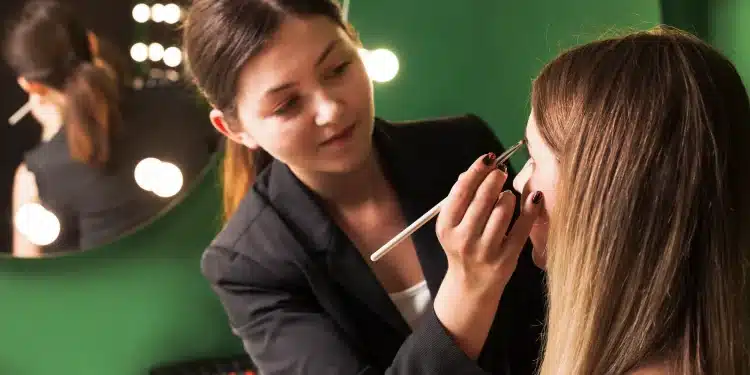 Profissional de beleza aplicando maquiagem em cliente em estúdio iluminado.