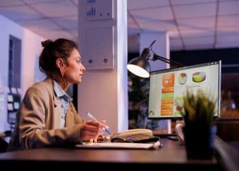 Profissional analisando gráficos financeiros em computador durante o trabalho noturno em escritório moderno.