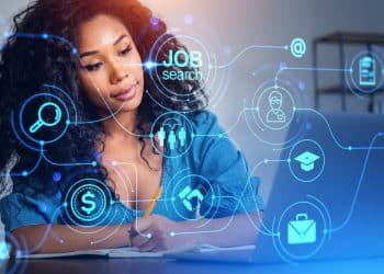 Jovem mulher negra com cabelo cacheado volumoso e escuro, vestindo uma camisa jeans azul claro. Ela está sentada à mesa, focada, com a mão direita segurando um lápis e apoiada em um caderno aberto à sua frente, enquanto olha para um notebook aberto à sua direita. Sobre a imagem, há uma interface tecnológica futurista e transparente com ícones circulares neon de cor azul ciano, incluindo um símbolo de cifrão ($), um ponto de interrogação dentro de um círculo, e o texto branco "JOB search" dentro de um círculo maior, conectados por linhas digitais a outros ícones como um aperto de mão, um capelo de formatura e um perfil de usuário. O fundo é um ambiente de escritório moderno, neutro e desfocado.