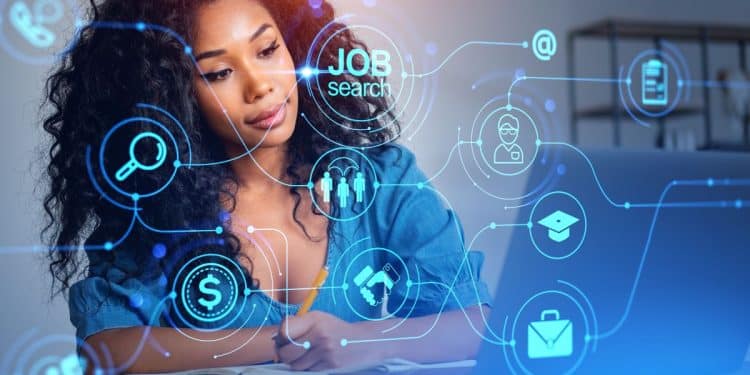 Jovem mulher negra com cabelo cacheado volumoso e escuro, vestindo uma camisa jeans azul claro. Ela está sentada à mesa, focada, com a mão direita segurando um lápis e apoiada em um caderno aberto à sua frente, enquanto olha para um notebook aberto à sua direita. Sobre a imagem, há uma interface tecnológica futurista e transparente com ícones circulares neon de cor azul ciano, incluindo um símbolo de cifrão ($), um ponto de interrogação dentro de um círculo, e o texto branco "JOB search" dentro de um círculo maior, conectados por linhas digitais a outros ícones como um aperto de mão, um capelo de formatura e um perfil de usuário. O fundo é um ambiente de escritório moderno, neutro e desfocado.