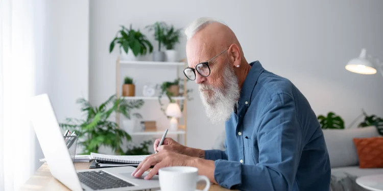 Homem maduro trabalhando no notebook em casa, representando renda extra online após os 50 anos.