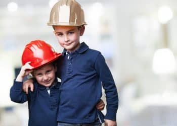 Duas crianças usando capacetes de obras coloridos abraçadas representando os sonhos de carreira e as profissões preferidas pelas crianças