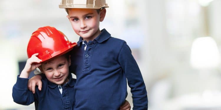Duas crianças usando capacetes de obras coloridos abraçadas representando os sonhos de carreira e as profissões preferidas pelas crianças