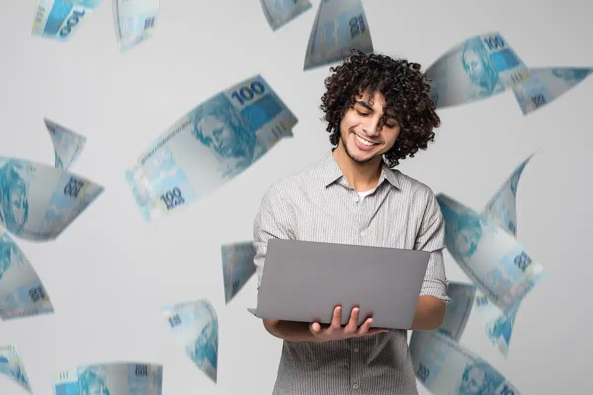 Profissional sorrindo enquanto trabalha em um laptop com notas de R$ 100 flutuando ao redor, representando uma carreira com alta renda e jornada reduzida.