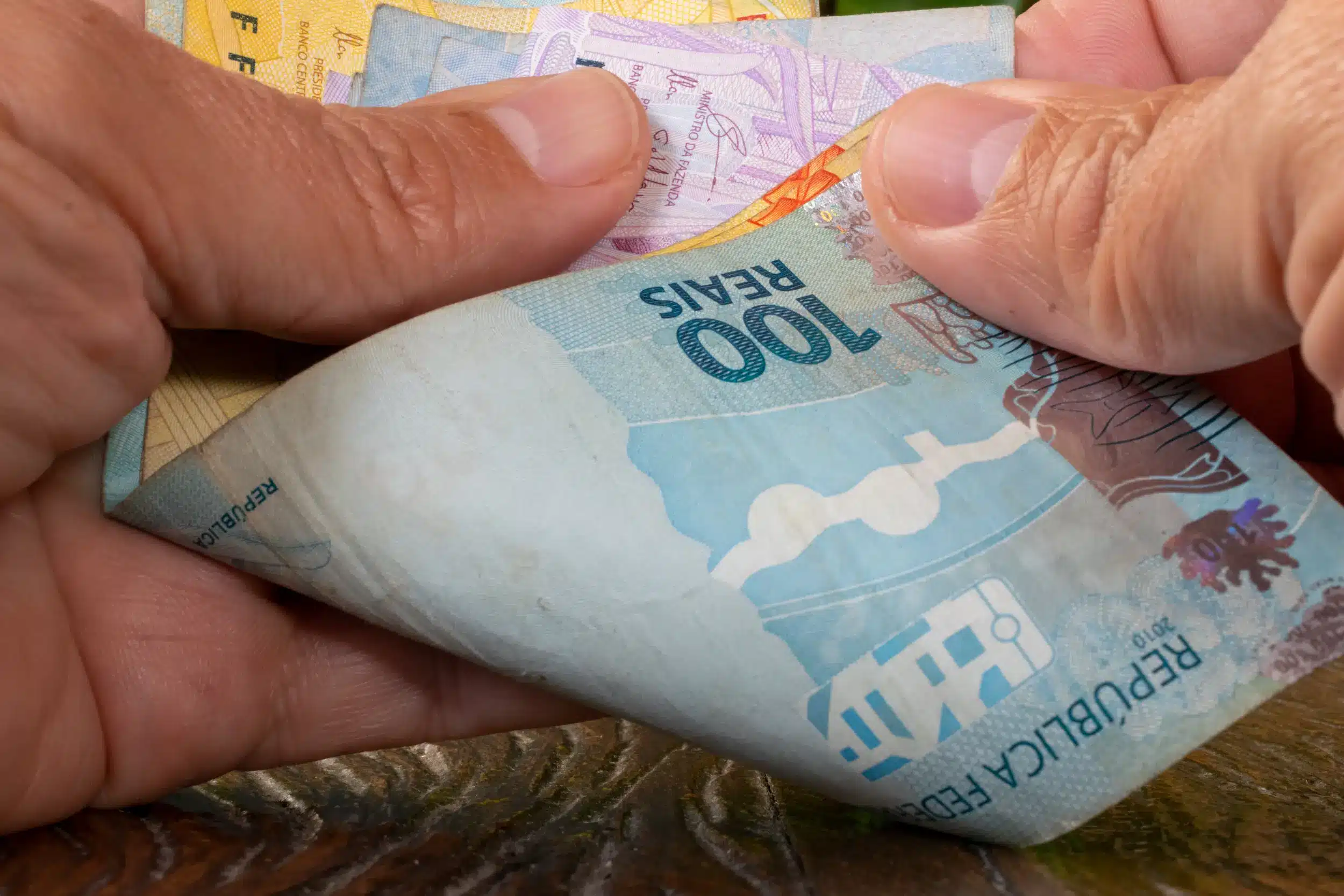 Notas de 100 reais sendo manuseadas, representando o alcance do salário ideal de até R$ 7.000 ou mais por meio de carreiras técnicas.