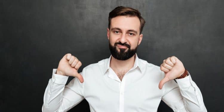 Homem de camisa branca fazendo gesto de polegar para baixo em fundo escuro, simbolizando frustração com baixos salários.