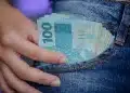 Notas de 100 reais sendo retiradas do bolso de um jeans, simbolizando o alcance do salário ideal no Brasil por meio de profissões técnicas.