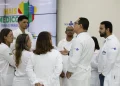 Grupo de médicos com jalecos brancos do SUS conversando em frente ao painel do programa Mais Médicos para o Brasil, representando os profissionais selecionados para atuar em regiões prioritárias do SUS
