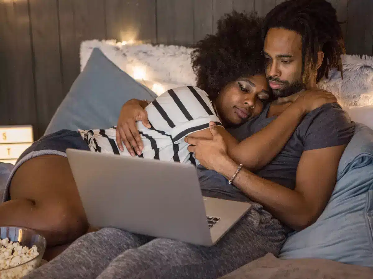 Casal abraçado assistindo a algo no computador, criando um ambiente acolhedor que facilita o sono rápido.