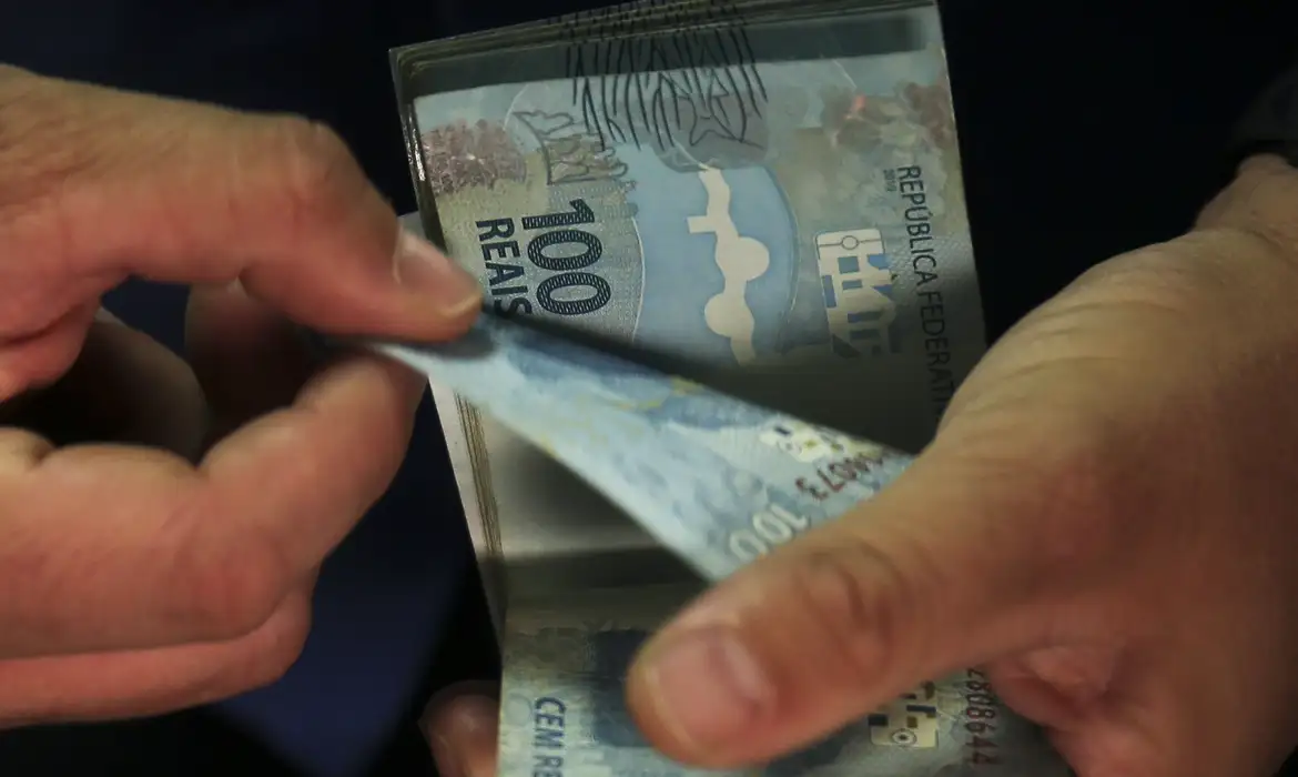 Pessoa contando notas de 100 reais referentes ao calendário do 13º do INSS
