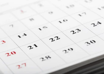 Calendário de parede em close com datas em preto e vermelho, sendo os números em vermelho indicando domingos e feriados, representando o calendário da Semana Santa 2026 e a dúvida sobre a Quinta-feira Santa ser ou não feriado nacional no Brasil