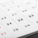 Calendário de parede em close com datas em preto e vermelho, sendo os números em vermelho indicando domingos e feriados, representando o calendário da Semana Santa 2026 e a dúvida sobre a Quinta-feira Santa ser ou não feriado nacional no Brasil