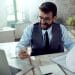 Profissional analisa documentos e utiliza celular em ambiente de escritório corporativo.