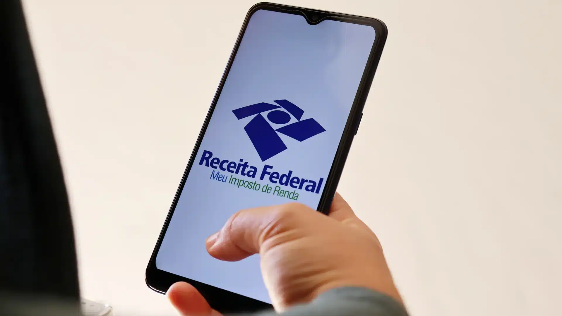 Mão segurando smartphone com tela do app Receita Federal exibindo logo e texto Meu Imposto de Renda