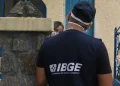 Agente do IBGE de costas, com colete de identificação do instituto, em frente a uma residência, representando o trabalho de campo realizado pelos candidatos aprovados no processo seletivo simplificado do IBGE