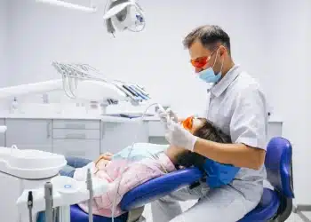 Dentista realizando procedimento odontológico em paciente mulher em consultório