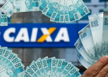 Cédulas de 100 reais em frente à agência da CAIXA, ilustrando o saque de R$ 6.220 para brasileiros.