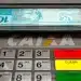 Notas de real sendo retiradas em caixa eletrônico da CAIXA durante liberação de benefício financeiro.
