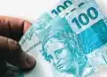 Mão segurando notas de R$ 100 em close, simbolizando o valor de até R$ 6.220 que trabalhadores residentes em cidades atingidas por desastres naturais podem sacar até o prazo final de 14 de abril de 2026.