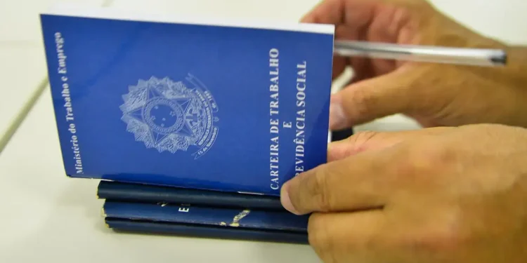 Mãos segurando a Carteira de Trabalho e Previdência Social com uma caneta, representando o processo de solicitação do seguro-desemprego em 2026