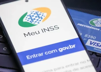 Tela de login do aplicativo Meu INSS aberta em um celular sobre teclado de notebook, ao lado de cartão da Previdência Social.