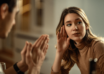Mulher loira de blusa bege ouve atentamente homem gesticulando durante diálogo íntimo