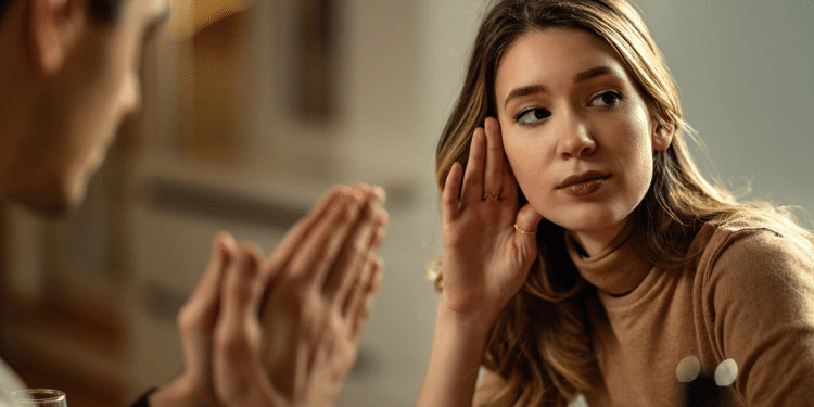 Mulher loira de blusa bege ouve atentamente homem gesticulando durante diálogo íntimo