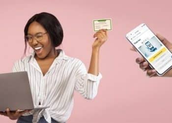 Jovem sorridente segura um Título de Eleitor enquanto utiliza um notebook, ao lado de uma mão exibindo um aplicativo de serviços eleitorais no celular.