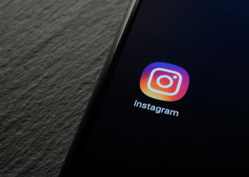 Ícone do Instagram com gradiente roxo, rosa e laranja exibido em tela de celular sobre superfície texturizada escura