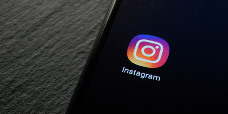 Ícone do Instagram com gradiente roxo, rosa e laranja exibido em tela de celular sobre superfície texturizada escura