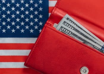 Carteira vermelha com notas de 100 dólares sobre a bandeira dos Estados Unidos, ilustrando o impacto do salário mínimo no país.