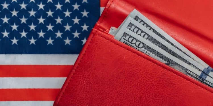 Carteira vermelha com notas de 100 dólares sobre a bandeira dos Estados Unidos, ilustrando o impacto do salário mínimo no país.