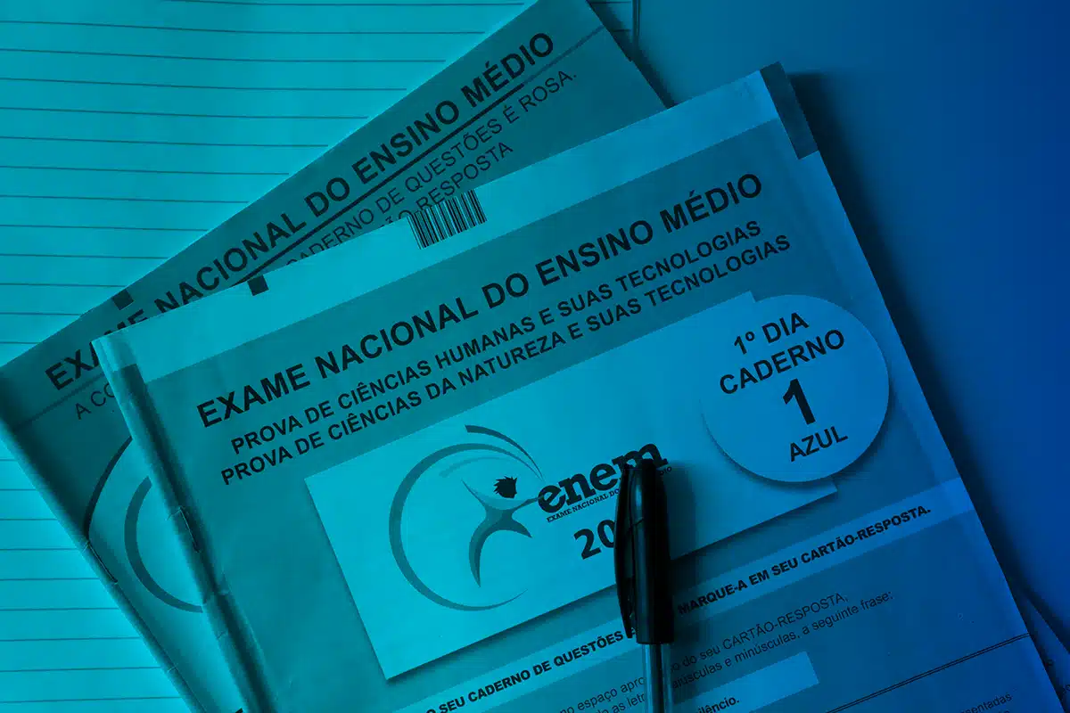 Cadernos de prova do Exame Nacional do Ensino Médio em destaque, com caneta sobre o material, representando a estrutura da aplicação do exame.