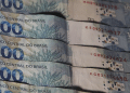 Notas de R$100 do Banco Central do Brasil sobrepostas em leque, exibindo tons azuis e verdes, simbolizando os pagamentos do 13º salário do INSS 2026.