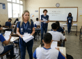 Aplicadores com coletes azuis distribuem provas para estudantes em sala de aula do Enem.