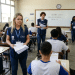 Aplicadores com coletes azuis distribuem provas para estudantes em sala de aula do Enem.