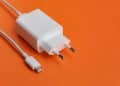 Carregador USB-C branco com cabo sobre fundo laranja vibrante.