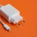 Carregador USB-C branco com cabo sobre fundo laranja vibrante.