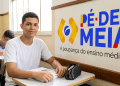 Jovem ao lado da logo do programa Pé-de-Meia.