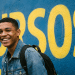 Jovem estudante sorridente em frente a muro com a palavra Cursos.