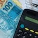 Cédulas de real brasileiro com calculadora e planilha financeira.