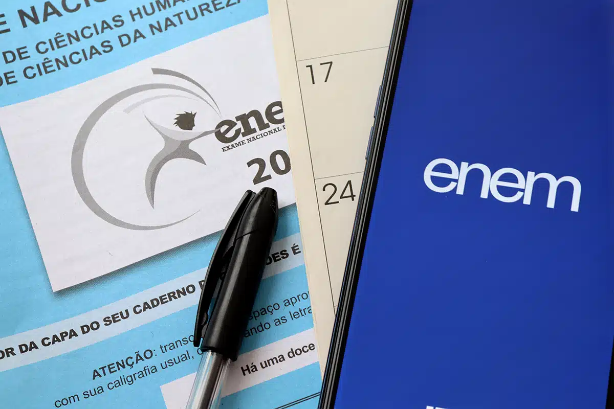 Caderno de provas e aplicativo do Enem com calendário ao fundo.