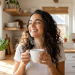 Mulher sorridente aprecia café quente em cozinha iluminada.