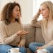 Duas amigas conversam em sofá.