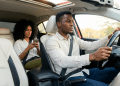 Mulher usando smartphone no banco do passageiro e homem dirigindo o carro.