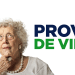 Idosa de cabelos cacheados com óculos e colar de pérolas pensativa ao lado do texto "Prova de Vida".